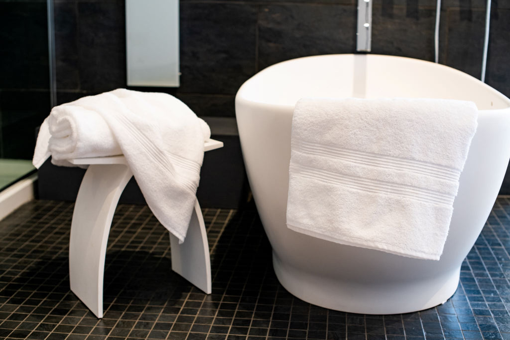 Thomaston Mills American Luxury Sustainable bath linens draped over a bath tub and folded and stacked on a stool.