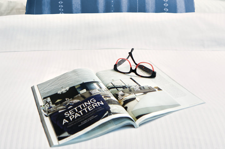 Bed made with Thomaston Mills American Luxury tonal stripe hotel bedding with a magazine laying on top.