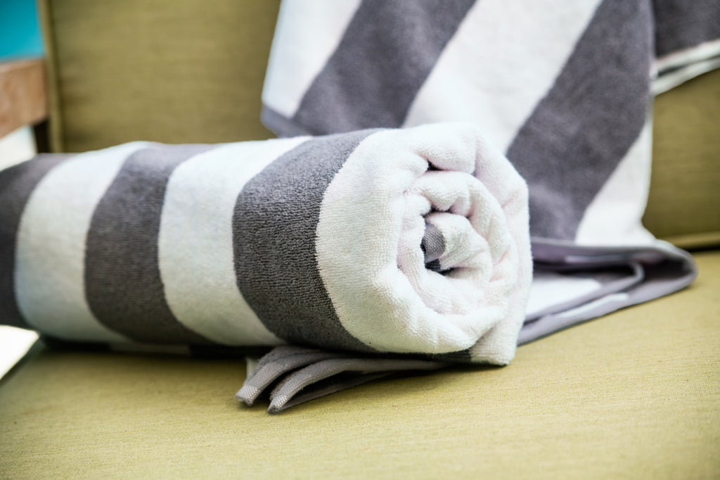 Thomaston Mills American Luxury Breeze gray and white pool towels rolled and stacked on top of a chair.