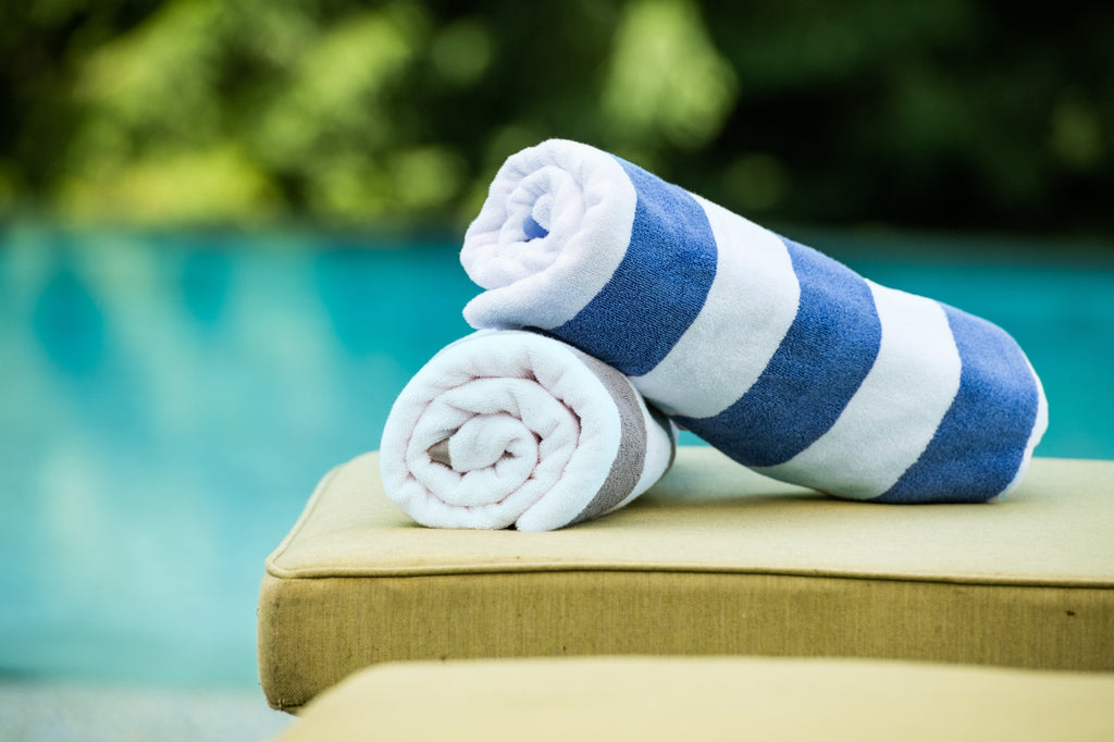 Thomaston Mills American Luxury Breeze blue and white pool towels rolled and stacked on top of a chair.